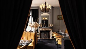 Uma sala de jantar com lareira, lustres e vista através de uma cortina.