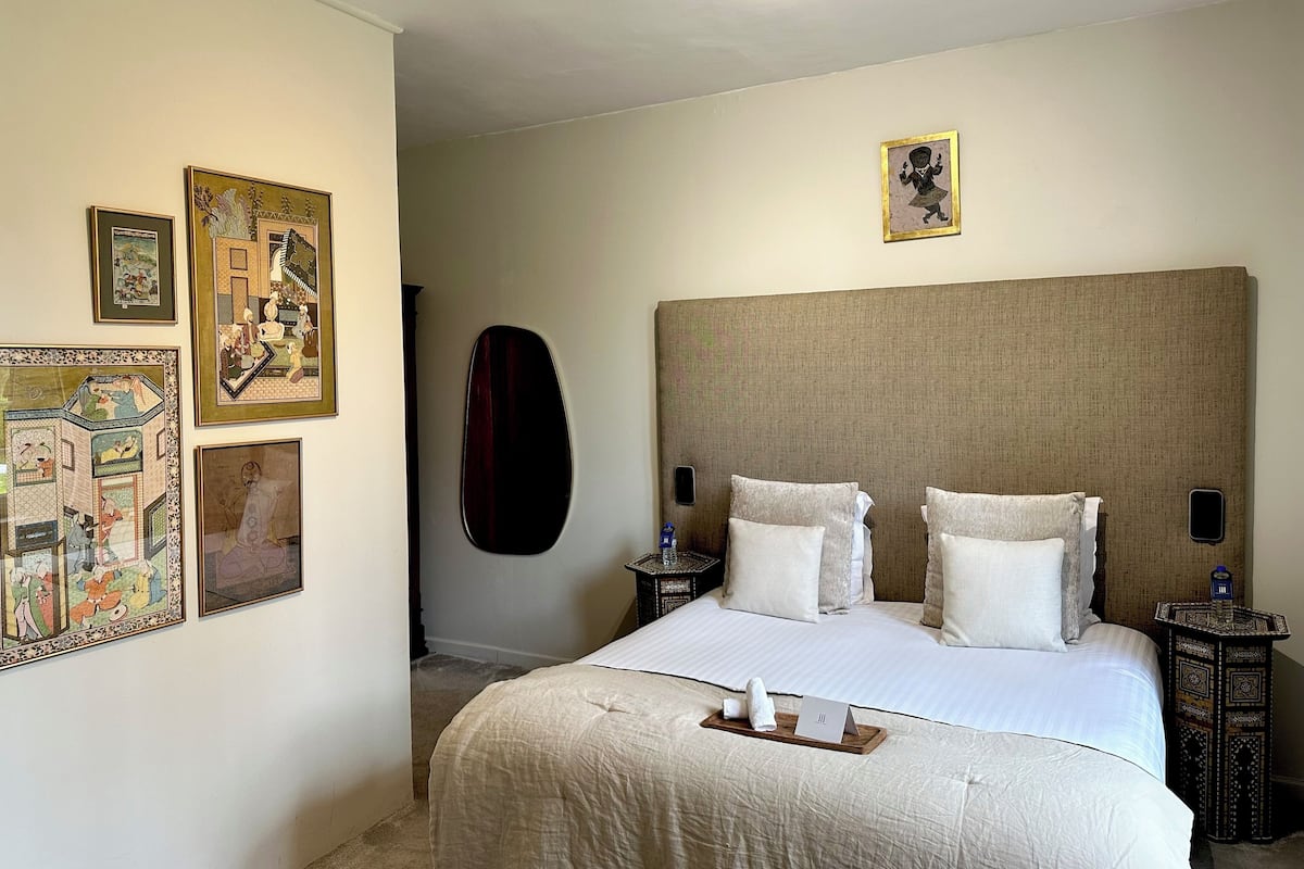 Quarto de hotel com uma cama grande, cabeceira e várias obras de arte emolduradas nas paredes.