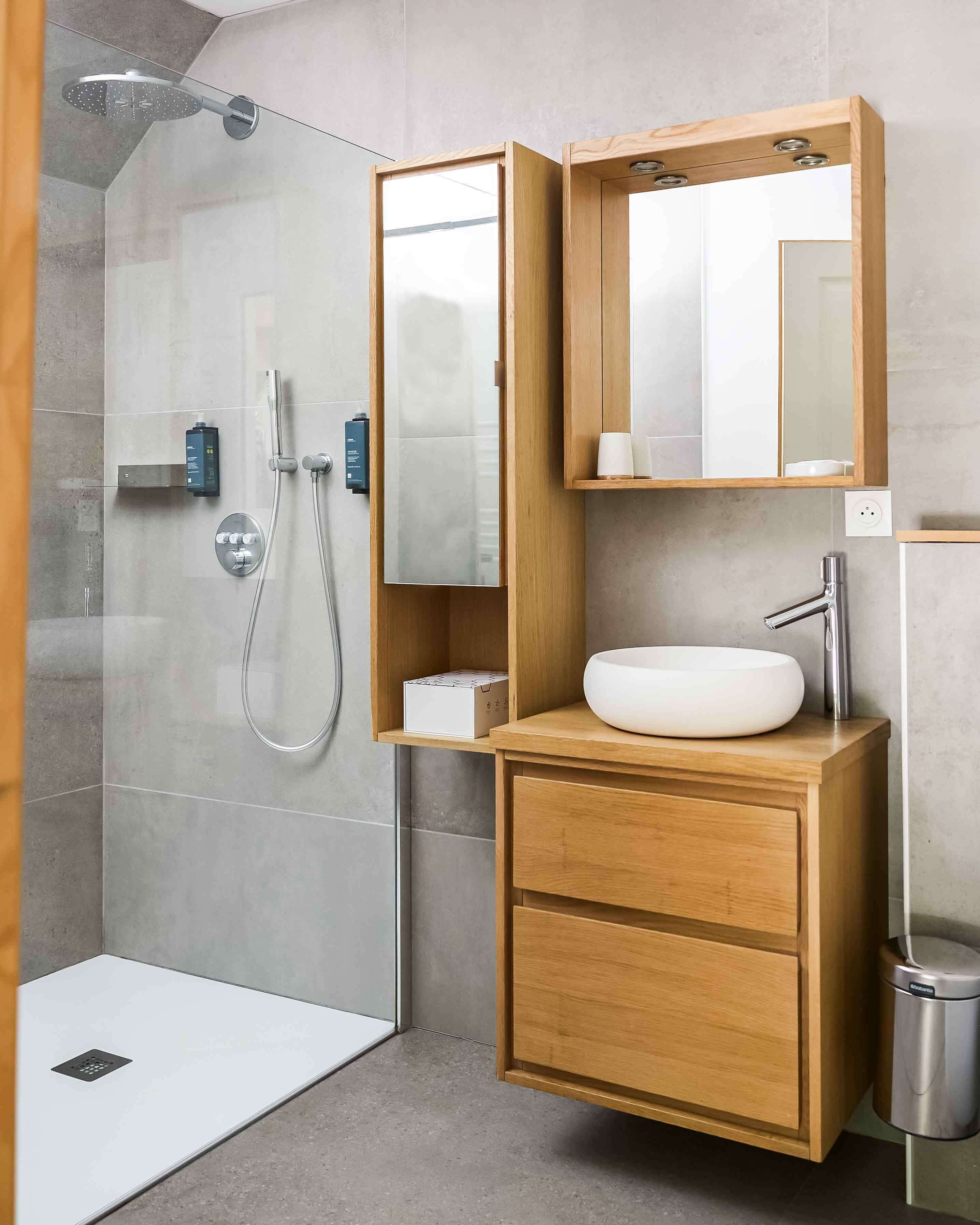 A modern bathroom with a glass shower enclosure, a wooden vanity with a sink, and a mirror above the vanity.