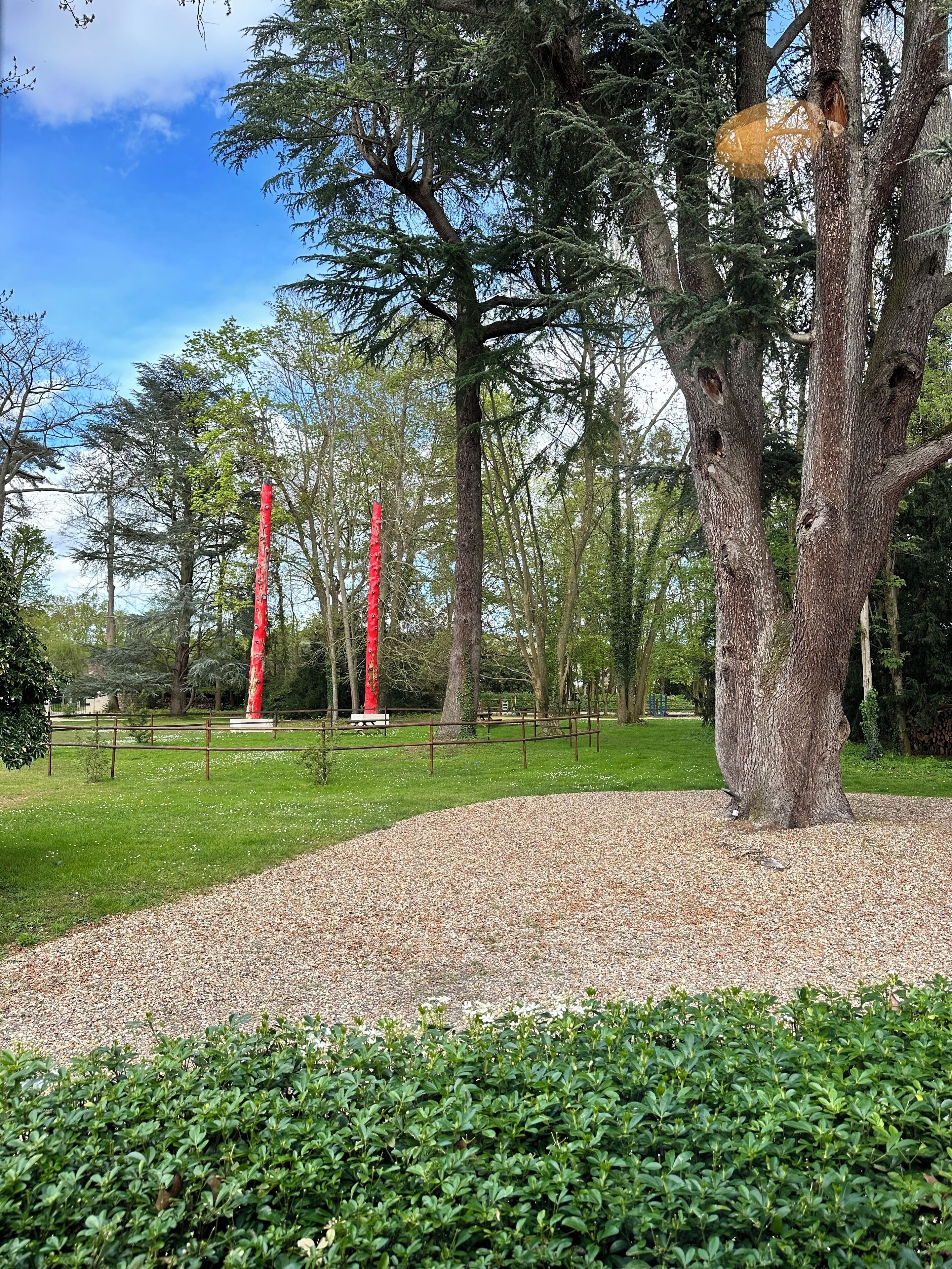 Un parque con un camino de grava, setos verdes y árboles altos.