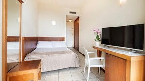 A hotel room with a bed, a desk with a TV, a chair, and a mirror. - Bellevue Beach (Cervia)
