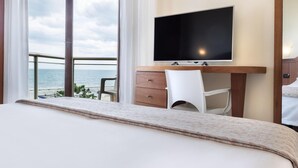 A hotel room with a bed, a desk with a flat-screen TV, a chair, and a view of the sea. - Bellevue Beach (Cervia)