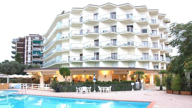 A multi-story hotel with a swimming pool and outdoor seating area. - Bellevue Beach (Cervia)
