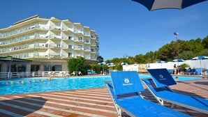 A poolside area with lounge chairs, a building with balconies, and umbrellas. - Bellevue Beach (Cervia)