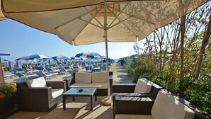 An outdoor seating area with wicker furniture and a large umbrella providing shade. - Bellevue Beach (Cervia)
