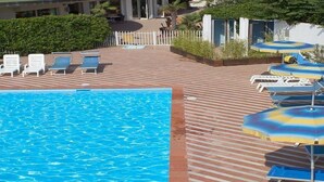 A pool area with a wooden deck, lounge chairs, and umbrellas. - Bellevue Beach (Cervia)
