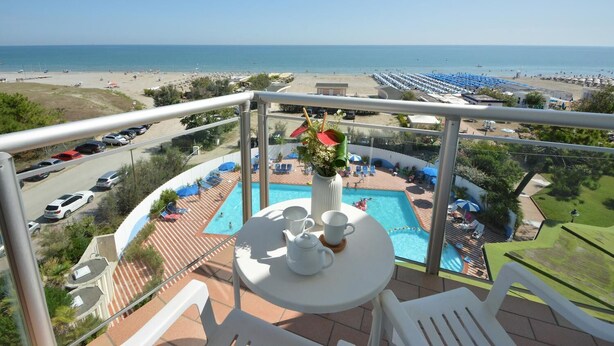 A balcony with a table, chairs, and a view of a pool and beach. - Bellevue Beach (Cervia)