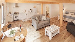 A spacious living area with a kitchen, a grey sofa, a coffee table, and a dining table with a wine bottle and glasses.