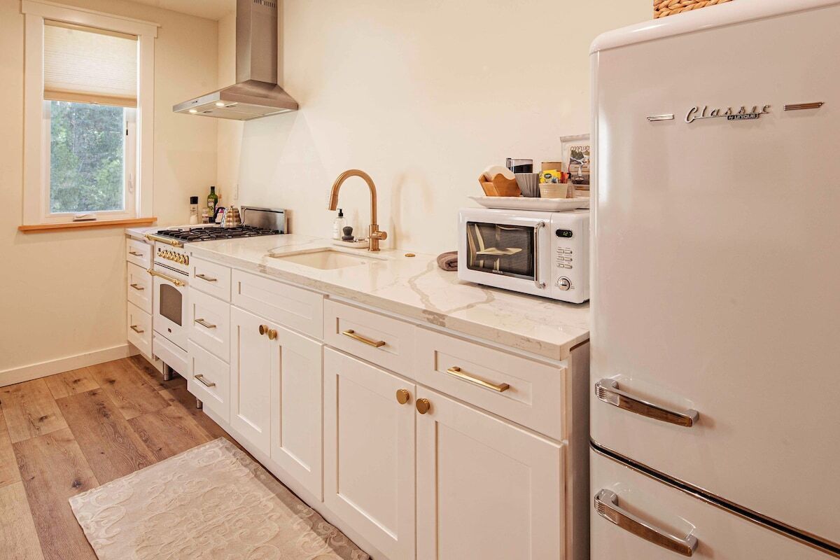 A kitchen with white cabinets, a stove, a sink, a microwave, and a refrigerator.