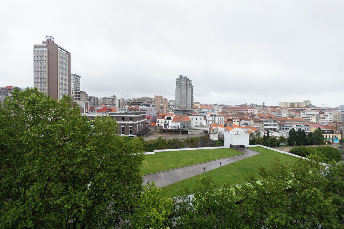Un paisaje urbano con una mezcla de edificios residenciales y comerciales, un edificio blanco destacado con una cúpula, y una amplia zona verde de parque.