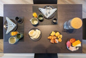 A neatly arranged breakfast table with plates of pastries, cheese, and meats, accompanied by cups and a glass of orange juice.