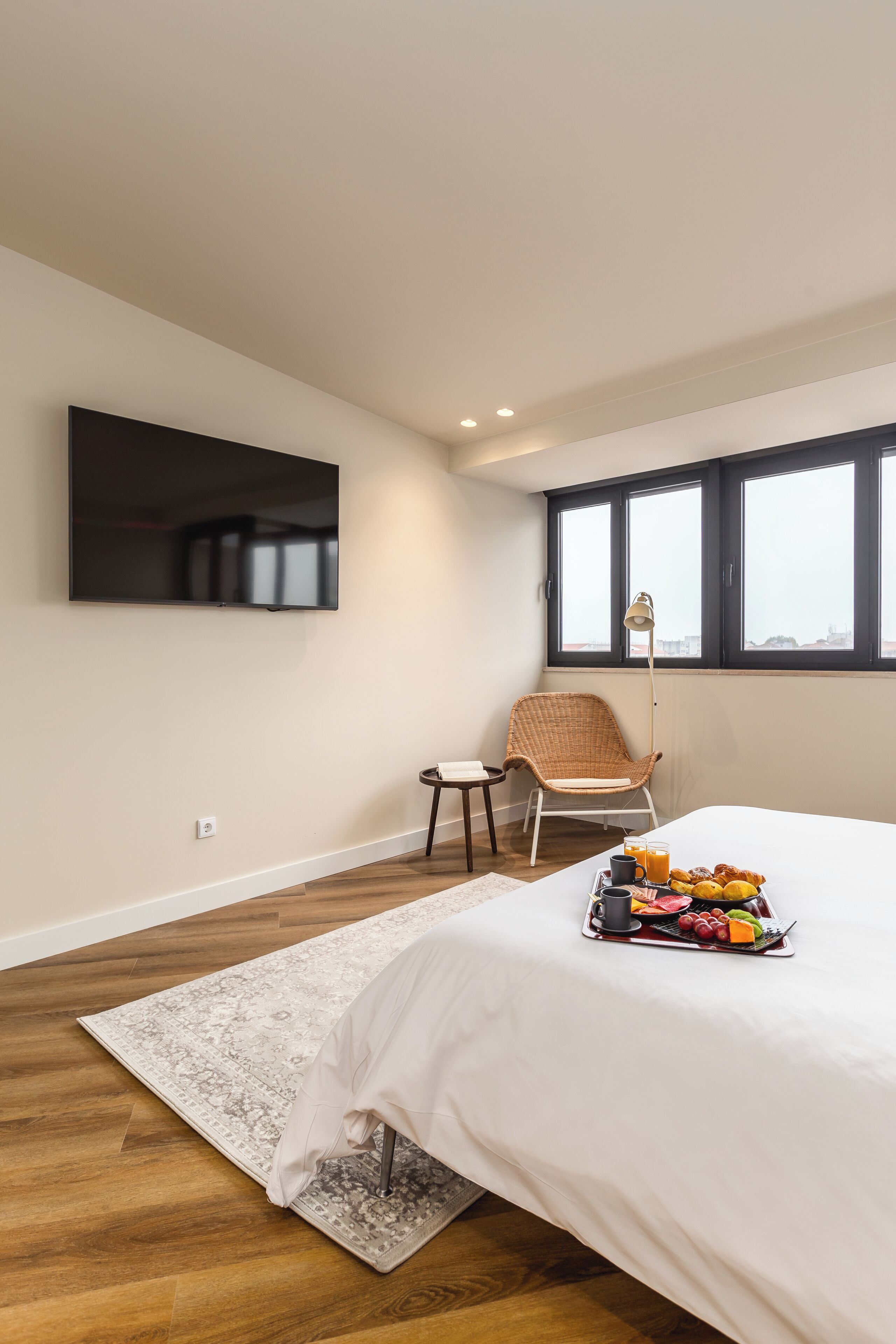 Ein Schlafzimmer mit einem Bett, einem an der Wand montierten Flachbildfernseher, einem Korbstuhl, einem kleinen Tisch und einem Fenster mit Blick.