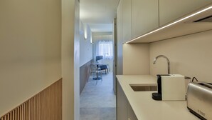 Una cocina moderna con un lavamanos integrado, un tostador y una tetera. Se aprecia un comedor con una mesa y sillas al fondo.