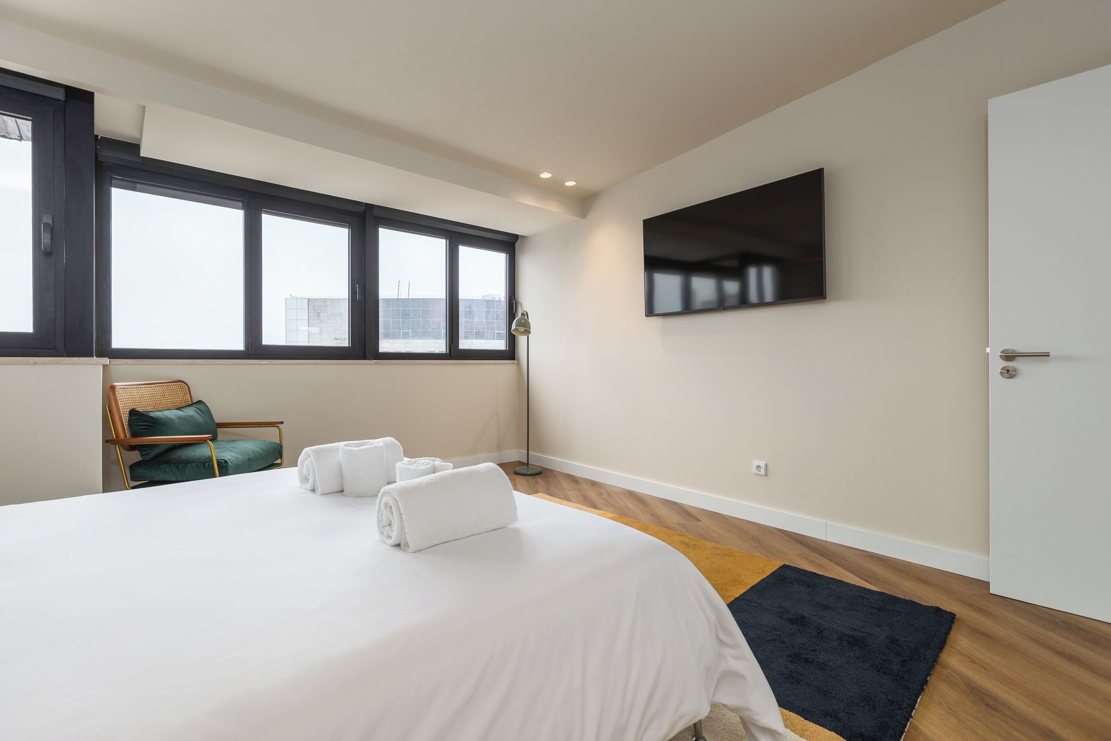 Una habitación de hotel moderna con una cama grande, un televisor de pantalla plana montado en la pared y una ventana con vistas a la ciudad.