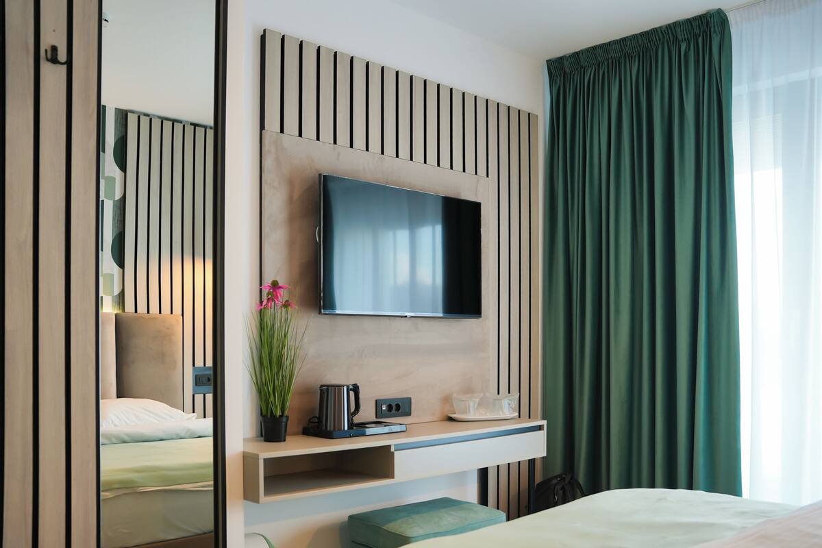 Habitación de hotel moderna con una pared de paneles de madera, televisor de pantalla plana, mesita de noche con una planta, cafetera y un pequeño estante.