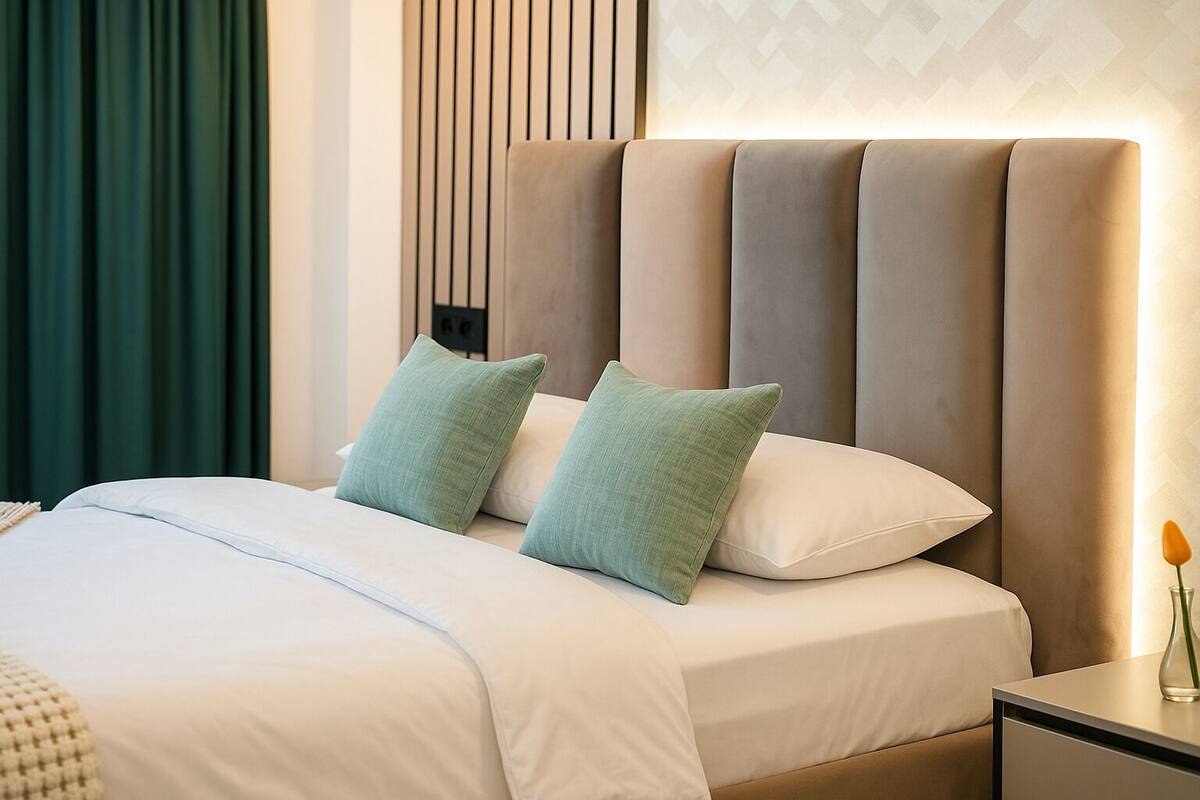Una cama bien hecha con dos almohadas, una mesita de noche con un florero y una pared con líneas verticales.