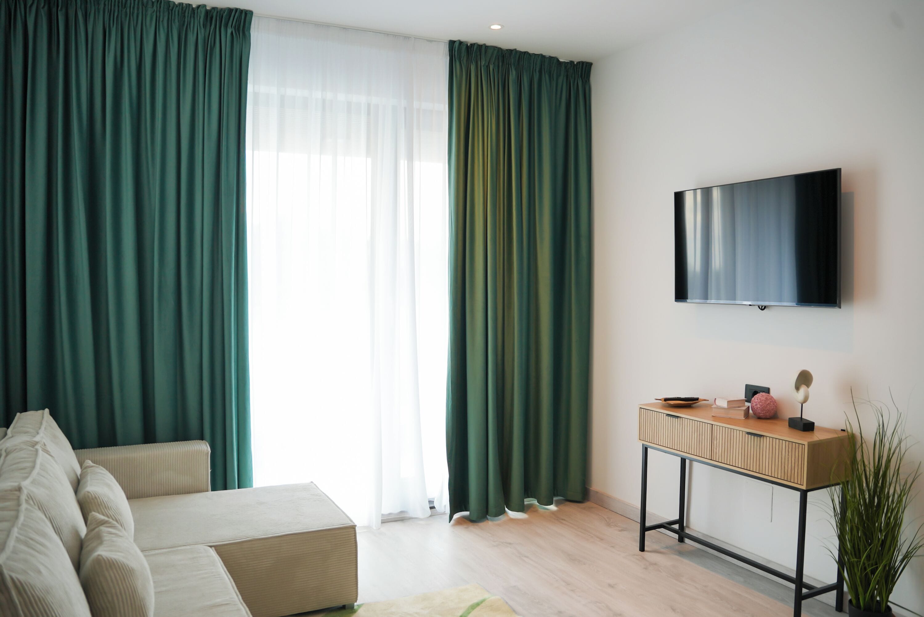 A modern living room with a sofa, a wooden side table, and a flat-screen TV mounted on the wall.