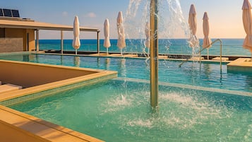 Un área de piscina con una fuente, sillas de descanso y sombrillas.