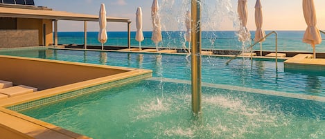 A pool area with a water fountain, lounge chairs, and umbrellas.