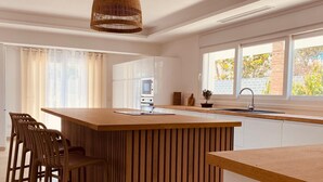 A modern kitchen with a central island, wooden chairs, a hanging light fixture, and a window with a view of greenery. - Villa Las Palmeras in Alhaurin de la Torre (Alhaurin de la Torre)
