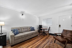 Ein Zimmer mit einer Couch, einem Esstisch mit Stühlen, einer Lampe und einer Tür.