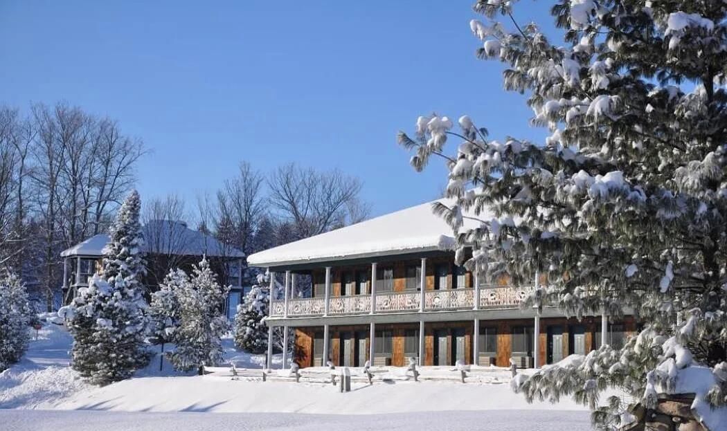Um edifício com varanda coberta e árvores cobertas de neve.