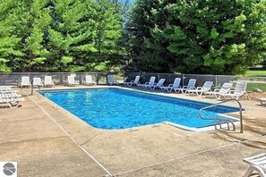 Piscina rectangular con escalera metálica, rodeada de sillas reclinables blancas.