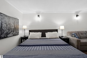Ein Hotelzimmer mit einem großen Bett, zwei Nachttischen mit Lampen, einem grauen Sofa und einem Bild an der Wand.