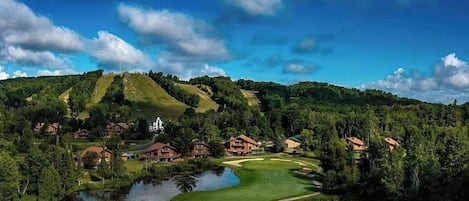 Camp de golf amb una bassa, envoltat de cases i un turó amb una església.