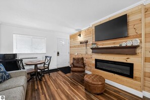 A living room with a fireplace, a flat-screen TV mounted on the wall, and a dining area with a table and chairs. - Condo in the Heart of Shanty Creek Resort! (Bellaire)