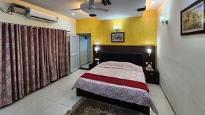A bedroom with a bed, a ceiling fan, an air conditioning unit, a door, a bedside table, and a nightstand.