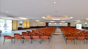 A conference room with rows of orange chairs, a podium, and a large screen at the front.