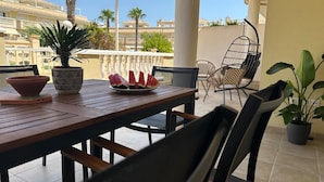 A patio with a wooden table, chairs, a bowl, a potted plant, and a plate of watermelon slices.