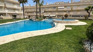 A swimming pool surrounded by a well-maintained lawn, palm trees, and a multi-story hotel building with balconies.