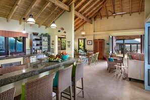 Un'ampia cucina con zona bar, sedie in vimini e zona pranzo con vista.