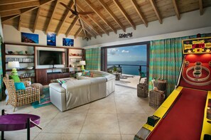 A spacious living area with a large TV, comfortable seating, a pool table, and a view of the ocean.