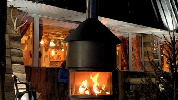 A wood-burning stove with a chimney, a stone fireplace, and a wooden bench outside a building. - Hôtel Restaurant Le Montlo 48 (Mont Lozere et Goulet)