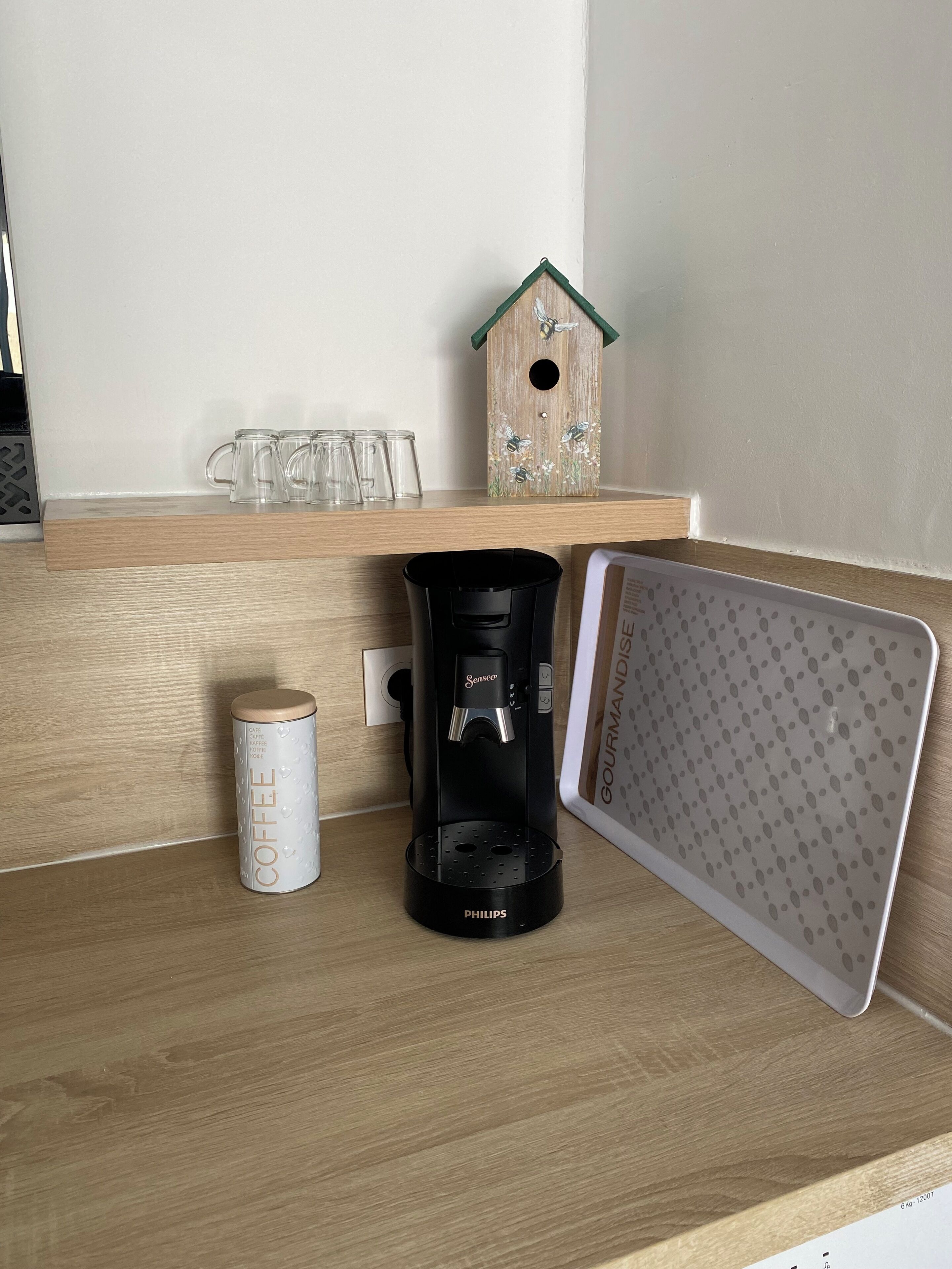 Eine Kaffeemaschine, eine Kaffeetasse und ein Vogelhäuschen auf einem Holzregal.
