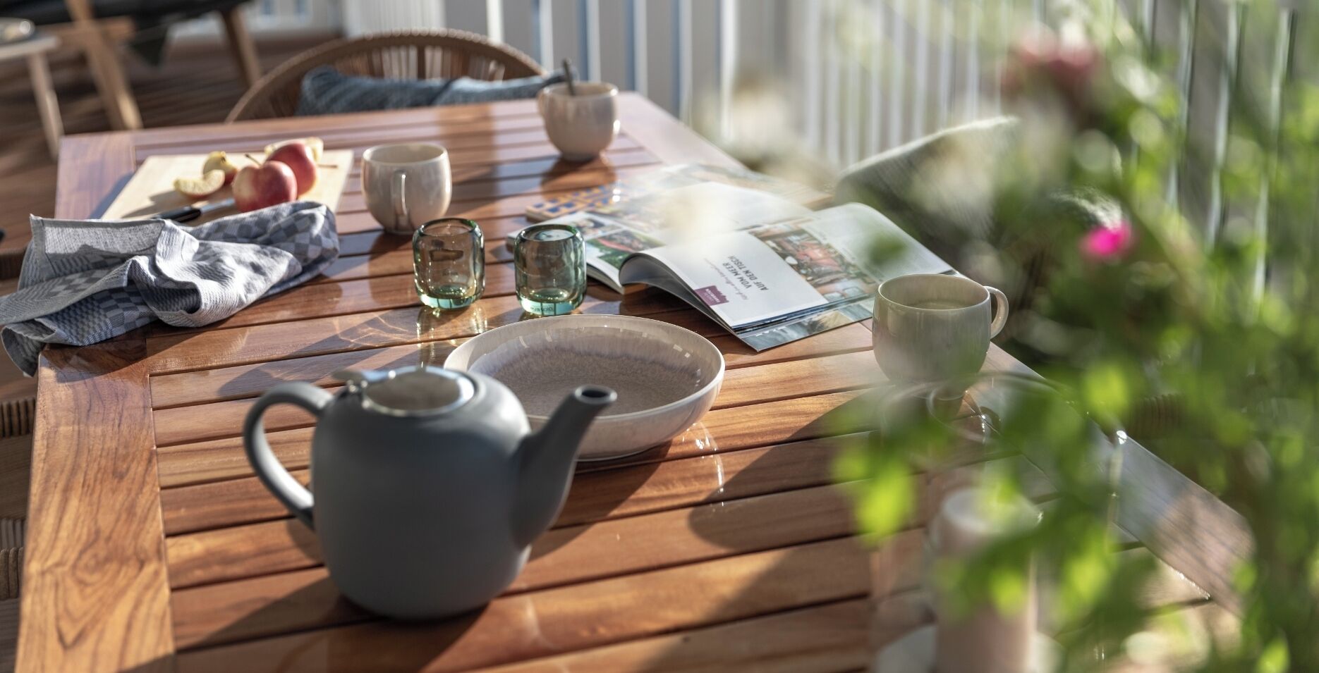 Une table en bois avec une théière, des tasses et un magazine.