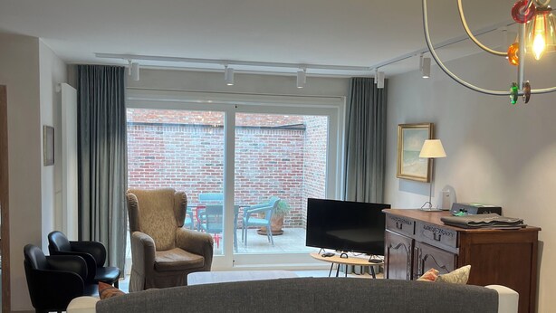Un salon moderne avec un canapé, des fauteuils, un téléviseur et un balcon donnant sur un mur en briques.