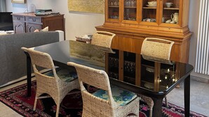 Un coin repas comprenant une table à plateau en verre, des chaises en osier, un buffet en bois doté de portes en verre et un lustre.