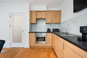 A compact kitchen with wooden cabinets, a built-in oven, a coffee machine, and a marble backsplash.