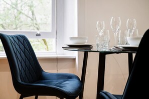 A dining table with a glass top, surrounded by chairs, in a room with a window.