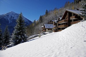 Eine Berglodge mit mehreren Balkonen, umgeben von schneebedeckten Bäumen und einer Bergkulisse.