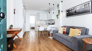 A modern living room with a grey sofa, wooden coffee table, and a dining area with white chairs and a small table.