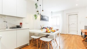 A modern kitchen with white cabinets, a marble countertop, and a dining area with a white table and wooden chairs.