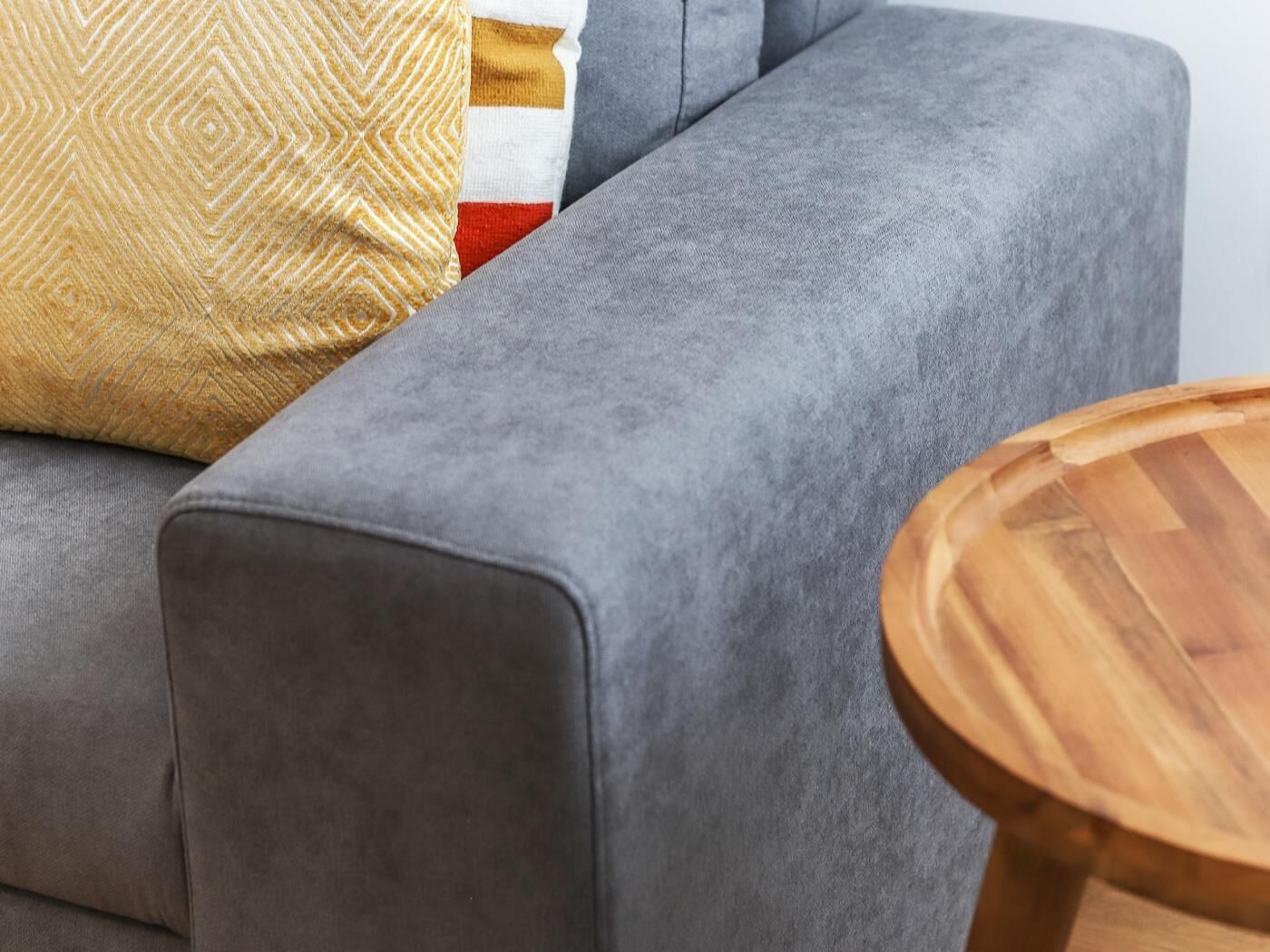 A grey sofa with a patterned throw pillow and a round wooden side table.