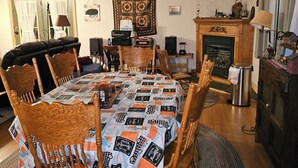 A dining room with a round table, wooden chairs, a patterned tablecloth, a ceiling fan, a fireplace, and a mirror. - Cabin stay close to state park (Spring Mills)