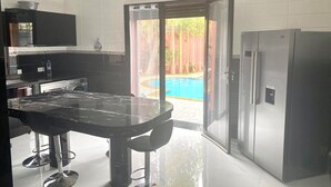 A modern kitchen with a large island, a refrigerator, and a view of a swimming pool. - Splendide Villa, Marrakech (Marrakech)