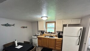 A compact kitchen with a stove, sink, and refrigerator. There is a dining table with chairs and a window above the sink. - Fishermen’s Denn, close to Lake Erie Islands, boat ramps, ferries, and marinas (Port Clinton)